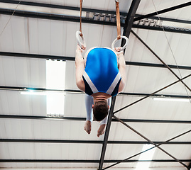 Image showing Man, acrobat and gymnast turning on rings in fitness for practice, training or workout at gym. Professional male gymnastics hanging on ring circles for athletics, balance or strength exercise indoors