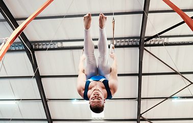 Image showing Man, acrobat and gymnastics upside down on rings in fitness for practice, training or workout at gym. Professional male gymnast hanging on ring circles for athletics, acrobatics or strength exercise