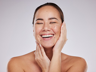 Image showing Skincare, hands on face and woman laughing in studio for cosmetics, dermatology and beauty glow. Happy aesthetic asian model person with makeup, skin mole and facial self care on grey background