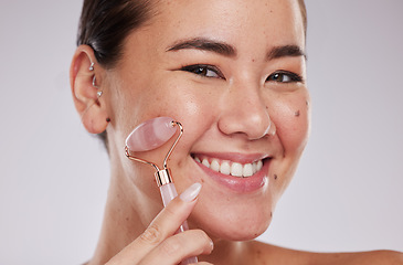 Image showing Face skincare, portrait and Asian woman with roller in studio isolated on gray background. Dermatology aesthetics, beauty and happy female model with rose quartz stone or crystal for skin health.