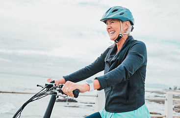 Image showing Senior woman, bike and smile in cycling by the beach for fun activity or travel in the city. Happy elderly woman smiling and enjoying cruise on bicycle for traveling, trip or fitness by ocean coast