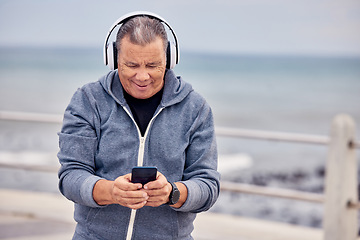 Image showing Music, phone and senior man by ocean for fitness, exercise and training for healthy lifestyle on promenade. Retirement, headphones and elderly male listening to audio, track or radio and texting