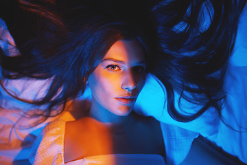 Image showing Portrait, vaporwave lights and young woman face in bedroom with creative disco lighting. Makeup, beauty and model resting and feeling relax and calm on a bed pillow with cyberpunk aesthetic