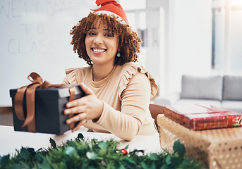 Image showing Christmas, box and portrait with a black woman teacher giving a gift at her desk in a school in a classroom. December, holiday and present with a female educator holding a giftbox while feeling happy