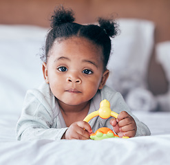 Image showing Cute, portrait and baby with a toy on her bed playing and relaxing in her modern nursery. Childhood, playful and African girl infant or newborn playing with plastic object in her bedroom at her home.