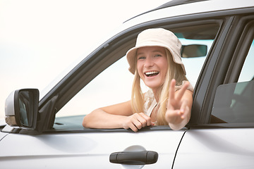 Image showing One beautiful blonde caucasian woman gesturing peace while enjoying a roadtrip. An attractive young female leaning out of the passenger window of a car while taking a drive. Enjoying the open road