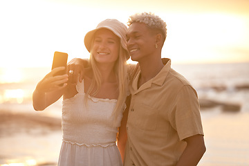 Image showing Closeup portrait of an young affectionate mixed race couple standing on the beach and smiling and taking a selfie with a smartphone during sunset outdoors. Hispanic man and caucasian woman showing l