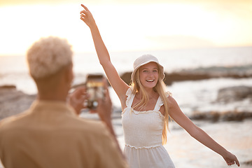 Image showing Mixed race boyfriend taking a photo of his caucasian girlfriend while having fun at the beach during sunset. Young couple having fun at the beach while using a wireless device