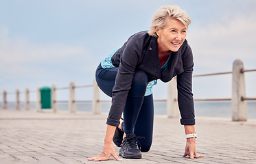 Image showing Senior woman, starting position and running outdoor at beach promenade, exercise or sky mockup. Elderly lady ready to run for fitness, cardio training and smile for sports marathon, health or mindset