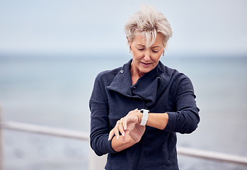 Image showing Smart watch, senior woman and fitness outdoor at beach promenade, exercise or sky mockup. Stopwatch, sports lady and runner check time, heart rate and monitor healthy body progress, clock or data app