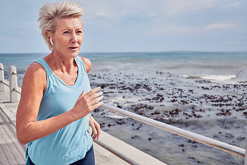 Image showing Senior woman, exercise and running at beach promenade, sky mockup or energy of health, wellness and workout. Elderly female, earphones and fitness at ocean of sports, cardio runner and strong mindset