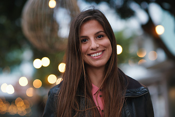 Image showing Portrait, smile and happy with a woman outdoor in the city during the evening on a blurred background. Face, holiday and travel with an attractive young female tourist standing out on the town