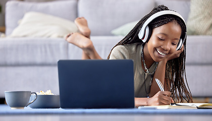 Image showing Black woman, student and laptop writing in book for elearning, education or entertainment in living room at home. Happy African American female with headphones taking notes by computer lying on floor