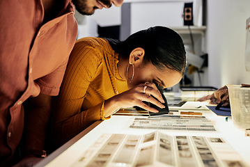 Image showing Photography, editing and film negatives for looking, magnifying glass or zoom analysis at photo journalist job. Photographer man, analyse or focus with woman in studio for creative choice in teamwork