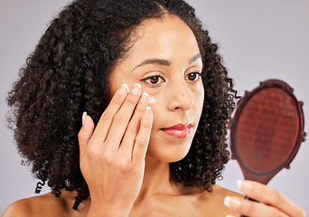 Image showing Face, skincare cream and black woman with mirror in studio isolated on a gray background. Dermatology cosmetics, reflection and female model with lotion, creme or moisturizer product for skin health.