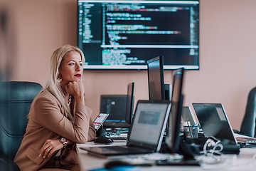 Image showing A businesswoman sitting in a programmer's office surrounded by computers, showing her expertise and dedication to technology.