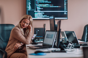 Image showing A businesswoman sitting in a programmer's office surrounded by computers, showing her expertise and dedication to technology.