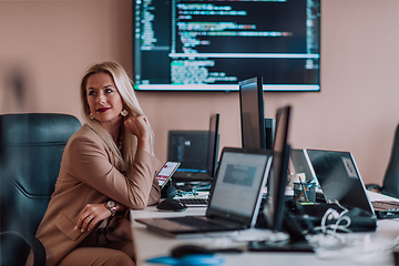 Image showing A businesswoman sitting in a programmer's office surrounded by computers, showing her expertise and dedication to technology.