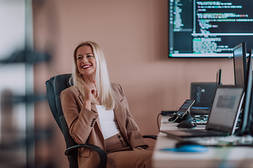 Image showing A businesswoman sitting in a programmer's office surrounded by computers, showing her expertise and dedication to technology.