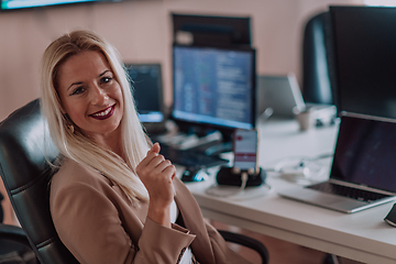 Image showing A businesswoman sitting in a programmer's office surrounded by computers, showing her expertise and dedication to technology.