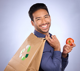 Image showing Man in portrait, happy and recycling paper bag with tomato and sustainable shopping on studio background. Eco friendly, vegetable and climate change awareness in retail, sustainability and health