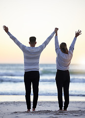 Image showing Couple, beach and hands up outdoor while happy at sunset for love, freedom and peace with calm ocean. Young man and woman together on vacation holiday at sea to relax, travel and connect in nature