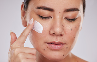 Image showing Skincare, facial and face cream for woman in studio for wellness, grooming and cosmetics on grey background. Sunscreen, model and asian girl relax with luxury beauty, skin and treatment with product