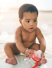 Image showing Kids, baby and black girl with a bottle sitting on a blanket on a home floor for child development. Children, cute and curious with a thirsty newborn infant learning or growing alone in a house