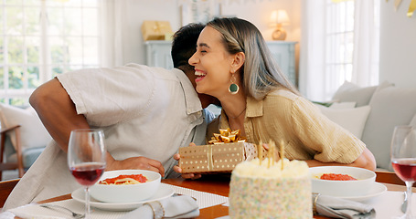 Image showing Interracial couple, gift and celebrate birthday being happy, kiss and smile in home at table with cake. Love, man and woman being content, romantic and present being cheerful celebration together.