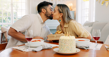 Image showing Interracial couple, gift and celebrate birthday being happy, kiss and smile in home at table with cake. Love, man and woman being content, romantic and present being cheerful celebration together.