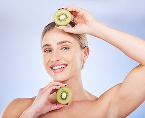 Image showing Portrait, kiwi and woman with skincare, cosmetics and smile with girl against a blue studio background. Face, female and lady with fruit, morning routine or grooming for smooth, clear or natural care