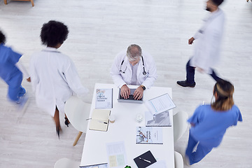 Image showing Doctor, man and laptop in busy hospital for medicine research, surgery schedule management or medical life insurance. Top view, healthcare worker and surgeon on technology with motion blur coworkers