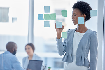 Image showing Black woman, writing and schedule for team planning or brainstorming tasks on glass board at the office. Serious African American female working on project plan, with sticky note for strategy