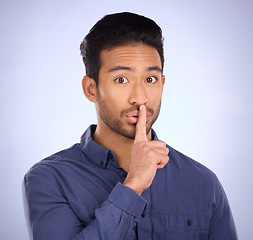 Image showing Man, portrait and finger on lips for secret, gossip or silence in studio with blue background. Face of a asian model person with hand on mouth for emoji sign to surprise, hush or quiet for privacy