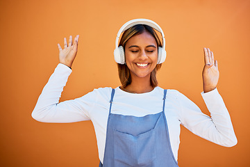 Image showing Music, dance and a young woman on an orange background in studio for freedom or fun. Radio, headphones and dancing with an attractive female streaming subscription service audio against a wall