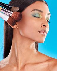 Image showing Makeup, brushes and Indian woman with foundation, facial treatment and girl against a blue studio background. Female, lady and tools for cosmetics, skincare and beauty for confidence and self care