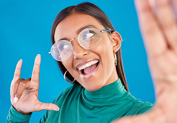 Image showing Woman, face and fashion selfie with rock on hand for gen z attitude on a blue background with glasses. Happy model person in studio with excited and cool hand sign or emoji with beauty and motivation