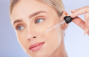 Image showing Face, beauty and skincare of woman with serum in studio isolated on a blue background. Dermatology cosmetics, thinking closeup and female model apply hyaluronic acid, retinol or essential oil product