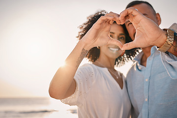 Image showing Love, couple and heart hands at beach on vacation, smile or having holiday fun. Ocean sunset, interracial romance and happy man and woman with affection emoji or gesture for care, trust or commitment