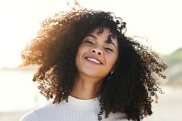 Image showing Black woman, afro and wind in hair outdoor with a smile and portrait at beach for vacation or freedom. Face of happy young model person in nature for peace, travel and time to relax on sunset holiday