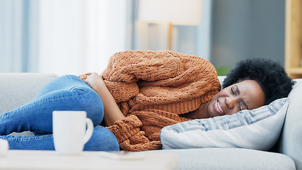 Image showing Woman with menstruation stomach cramps and belly ache holding her sore tummy while feeling ill on a sofa at home. Hungry female with period getting sick, bloated and uncomfortable with digestive pain