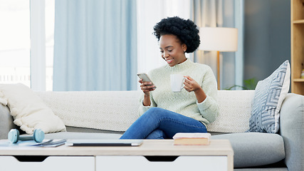 Image showing Happy African American woman texting on a phone while relaxing on a sofa and drinking coffee at home. Smiling black woman browsing social media and laughing, planning on how to spend her free time