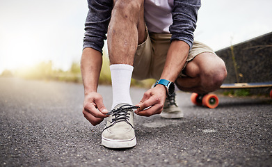 Image showing Hands, shoes and skate with a man tying his laces while on an asphalt skateboard for fun or recreation. Road, training or footwear with a male skater outdoor on a street while fastening his shoelaces