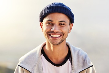 Image showing Portrait, happy and nature with a man in a beanie, standing outdoor in the wilderness on a gray sky. Face, smile and lifestyle with a handsome young male outside for travel, freedom or adventure