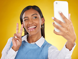 Image showing Selfie, face and peace with a woman in studio on a yellow background to post a profile picture update. Phone, social media and hand gesture with an attractive young female posing for a photograph