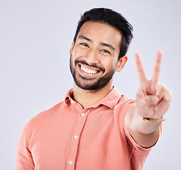 Image showing Portrait, smile and peace sign of Asian man in studio isolated on a gray background. Face, v hand emoji and happy, smiling and excited, young and confident male model with gesture or peaceful symbol.