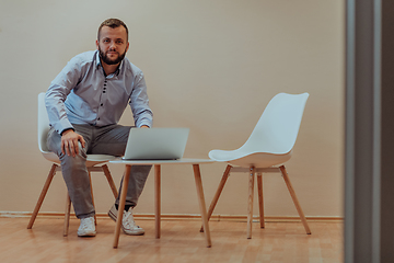 Image showing A confident businessman sitting and using laptop with a determined expression, while a beige background enhances the professional atmosphere, showcasing his productivity and expertise.