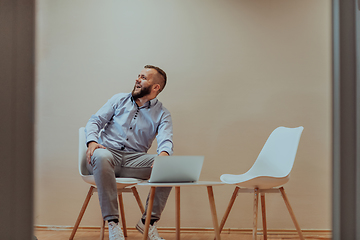 Image showing A confident businessman sitting and using laptop with a determined expression, while a beige background enhances the professional atmosphere, showcasing his productivity and expertise.