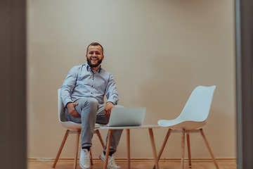 Image showing A confident businessman sitting and using laptop with a determined expression, while a beige background enhances the professional atmosphere, showcasing his productivity and expertise.