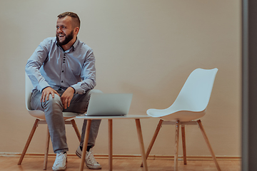 Image showing A confident businessman sitting and using laptop with a determined expression, while a beige background enhances the professional atmosphere, showcasing his productivity and expertise.